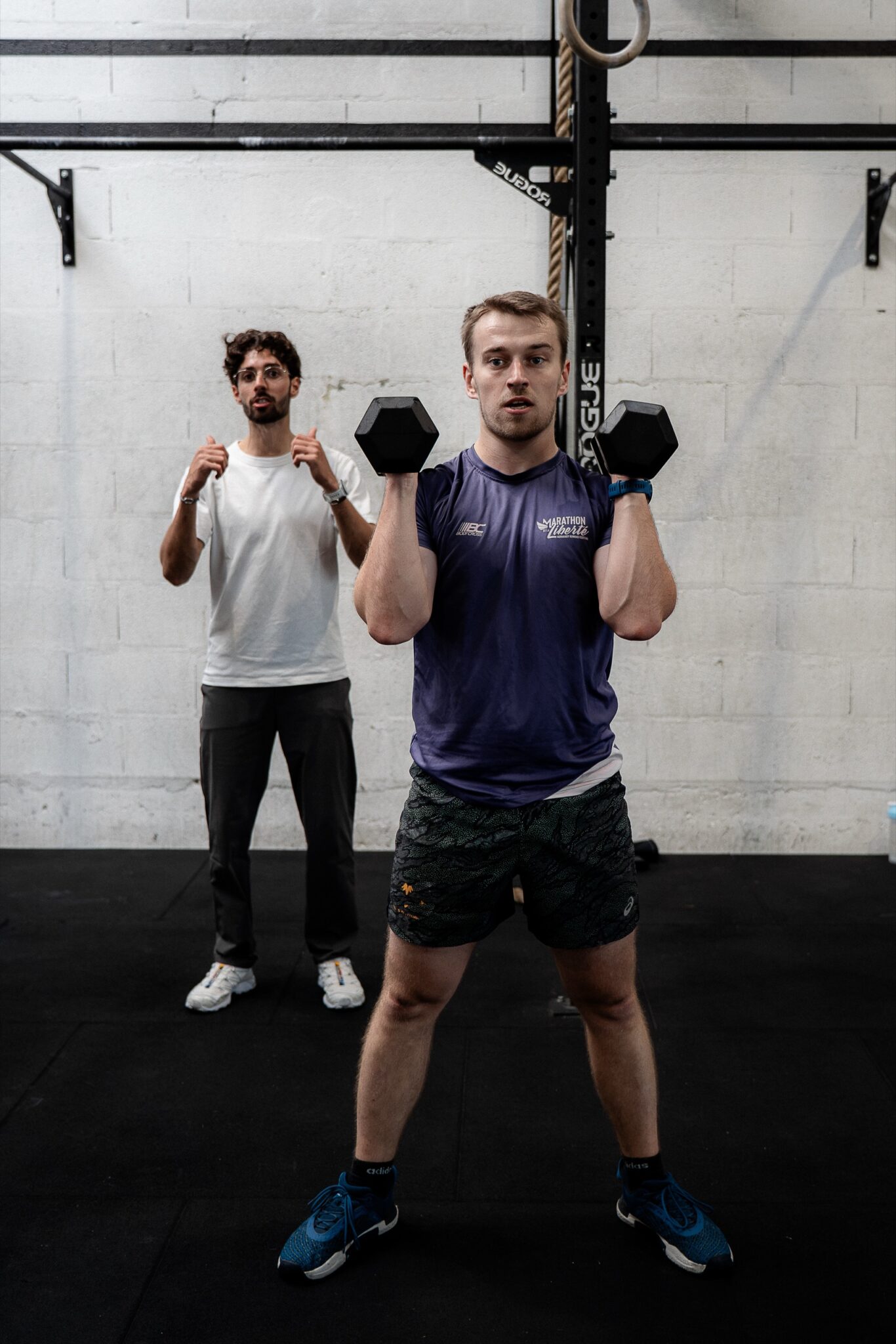 Un coach suit un adhérent pendant un front squat aux haltères, en séance individuelle